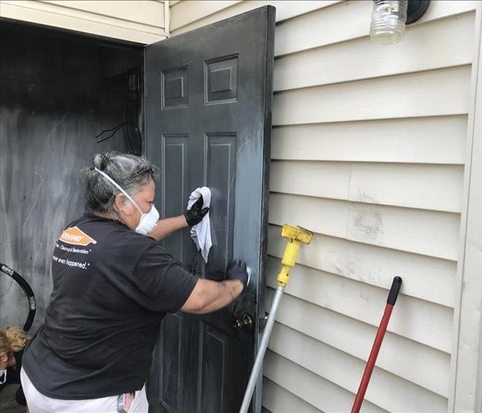 Female SERVPRO employee wearing a mask wipes down a soot-covered door