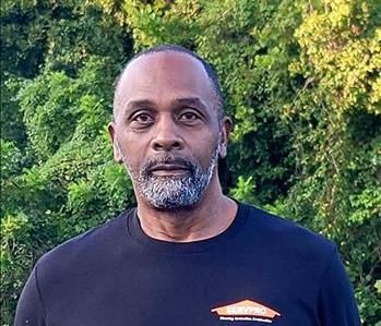 Headshot of man half-smiling man wearing black SERVPRO t-shirt in front of a gray backgound